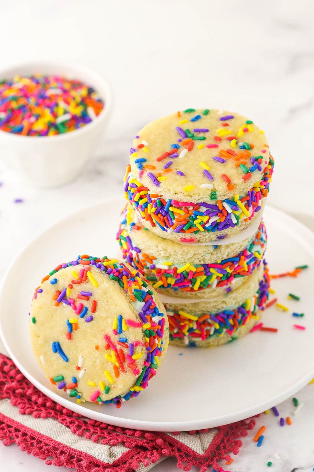 A stack of three ice cream sandwiches with another one beside them and a bowl of sprinkles in the background