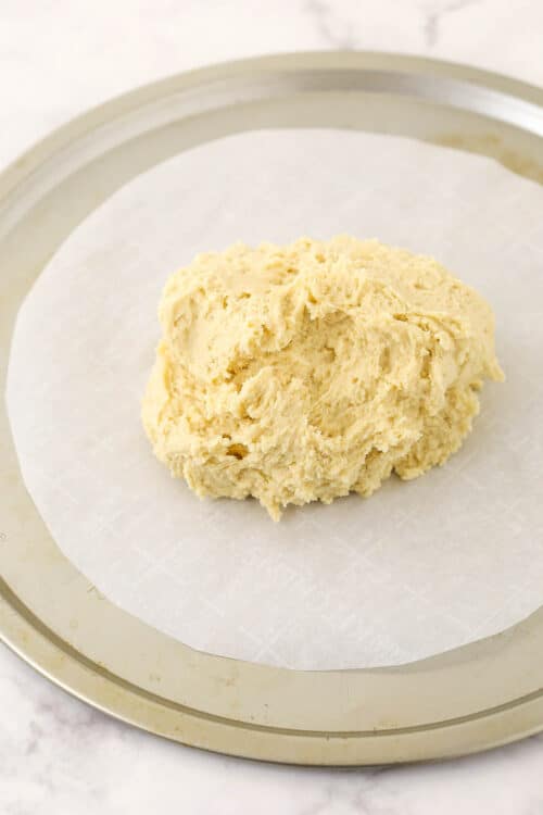 A ball of sugar cookie dough on a round pan lined with a circle of parchment paper