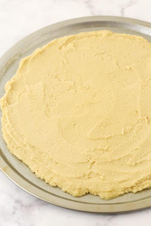 A circle of sugar cookie dough on top of a metal pizza pan