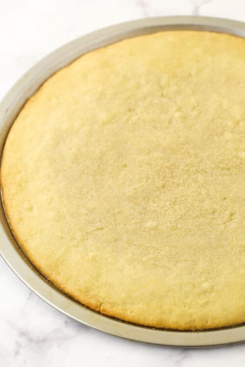 A baked and cooled sugar cookie crust inside of a parchment-lined pizza pan