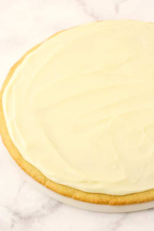 A round sugar cookie crust with an even layer of cream cheese buttercream frosting spread on top of it