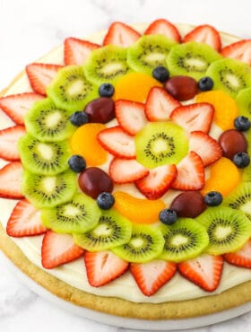 A fully decorated fruit pizza placed on a marble kitchen countertop