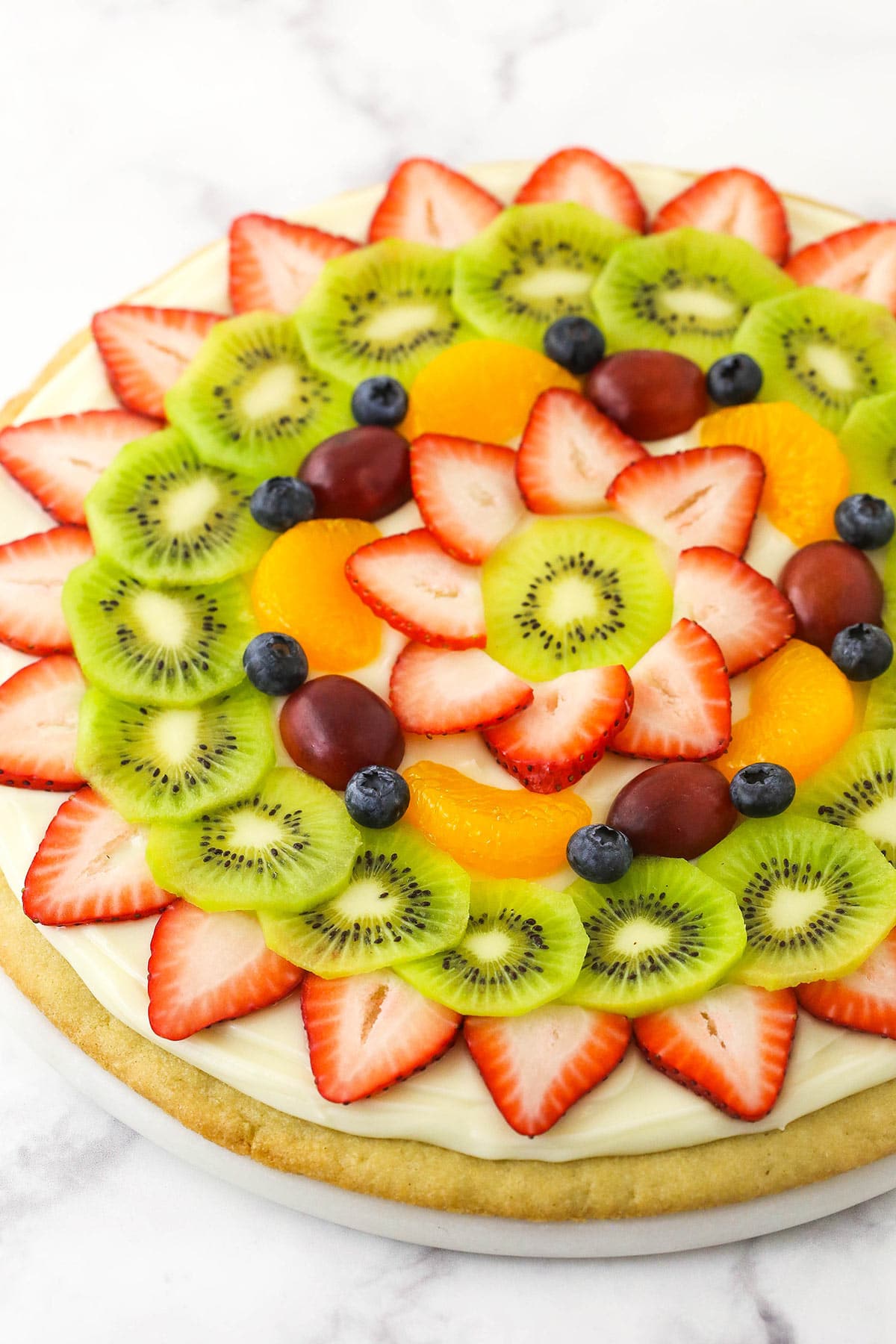 A fully decorated fruit pizza placed on a marble kitchen countertop