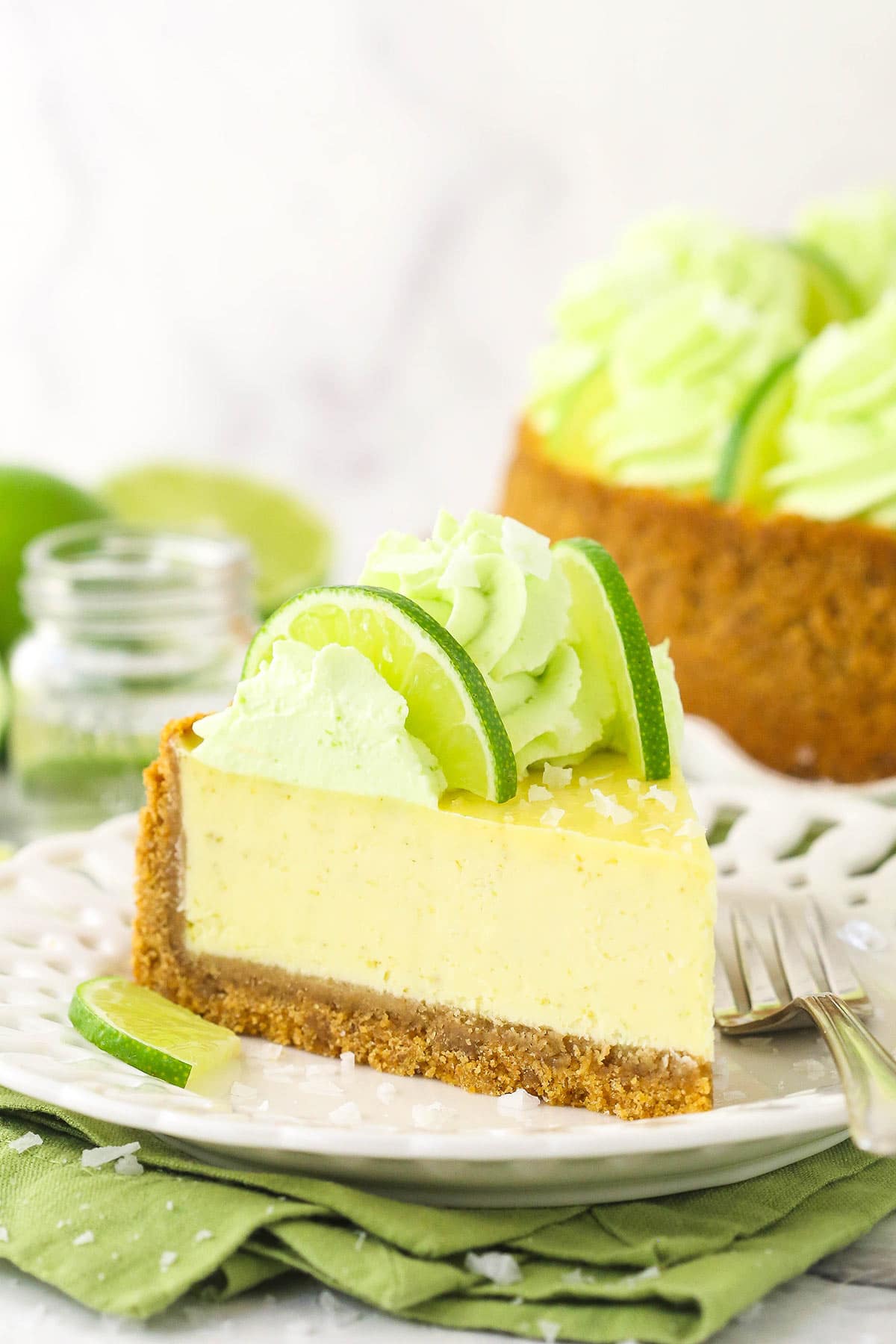 A piece of tequila lime cake on a dessert plate with a shot of tequila in the background