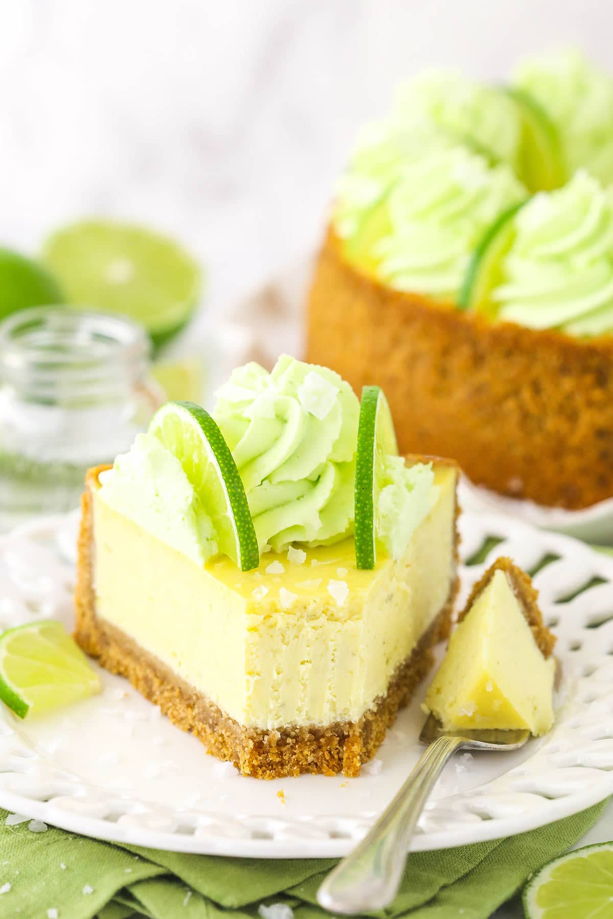 A slice of margarita cheesecake on a plate with one bite on a metal fork