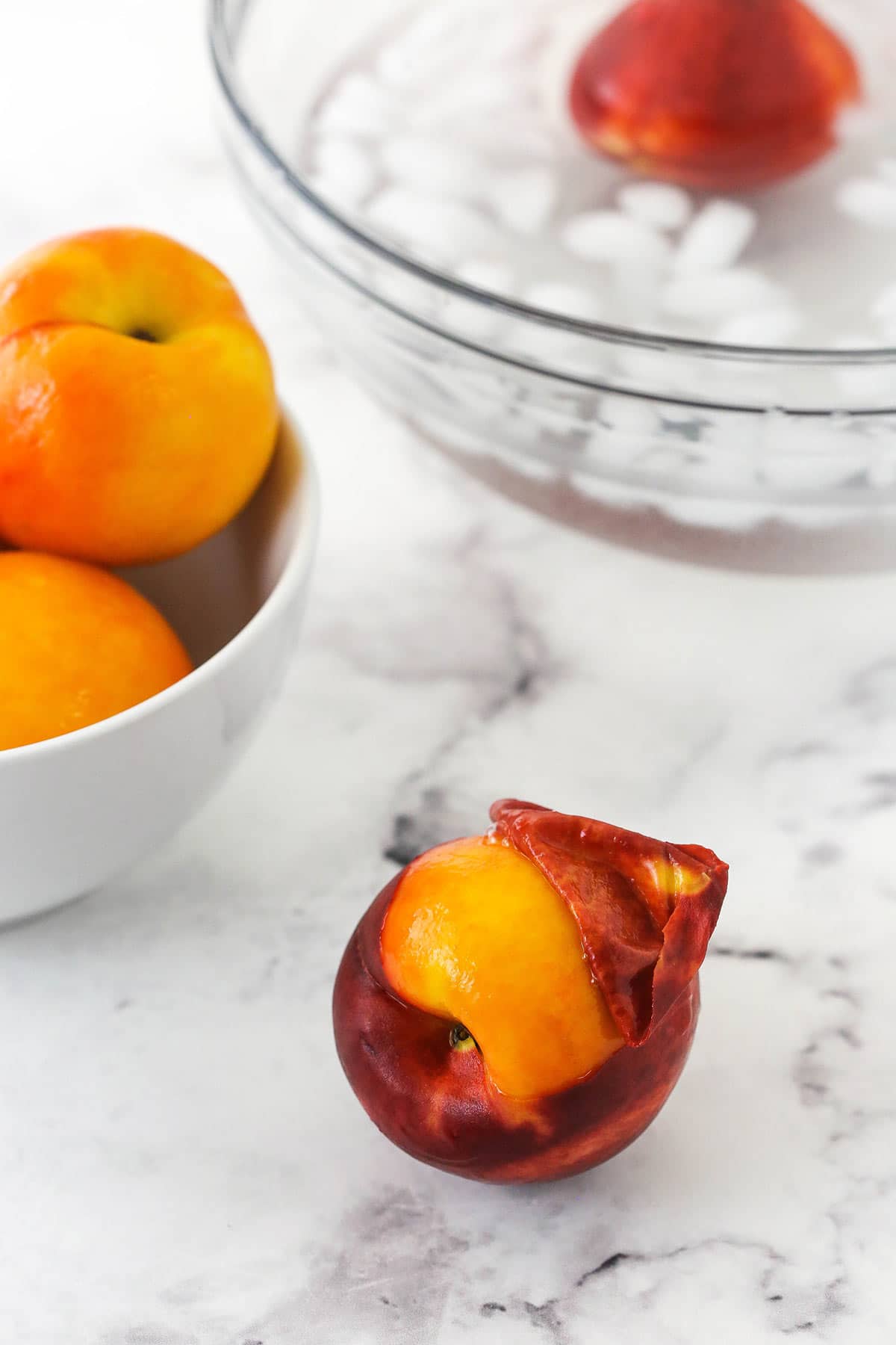 a peach being peeled sitting on marble table with ice bath and peaches in background