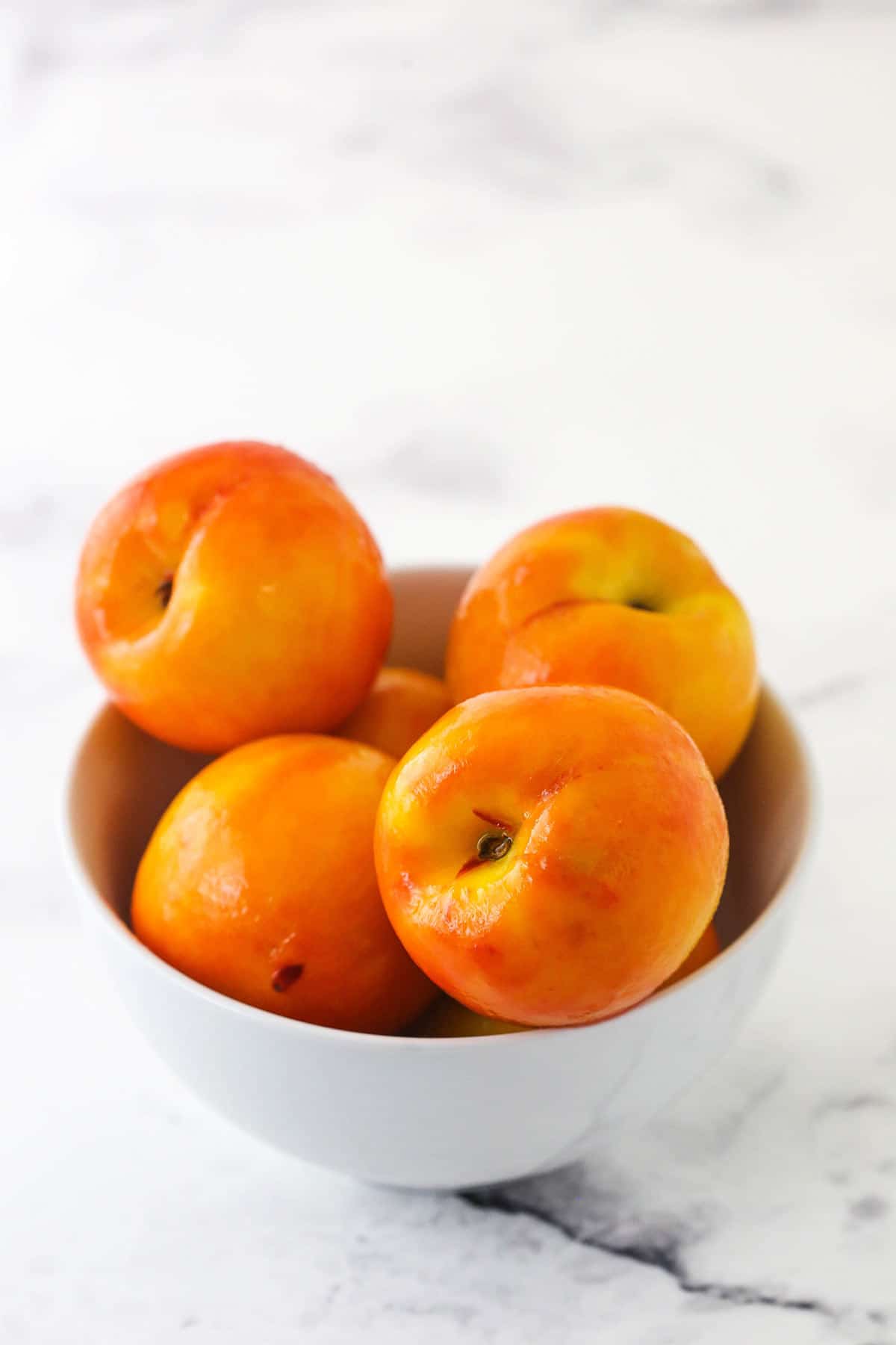 A while bowl full of peeled peaches on marble table