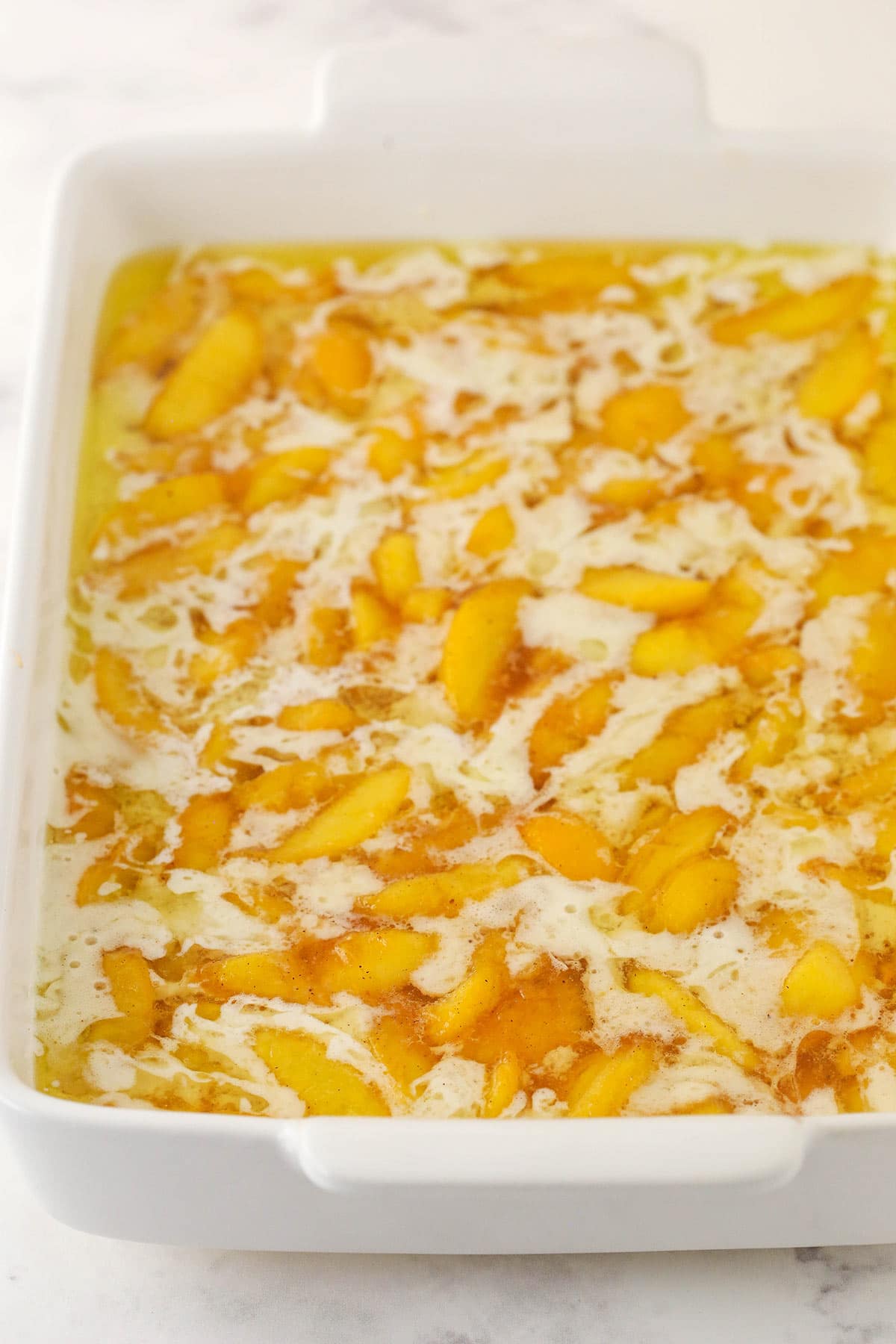 melted butter, batter and peaches all added to the casserole pan