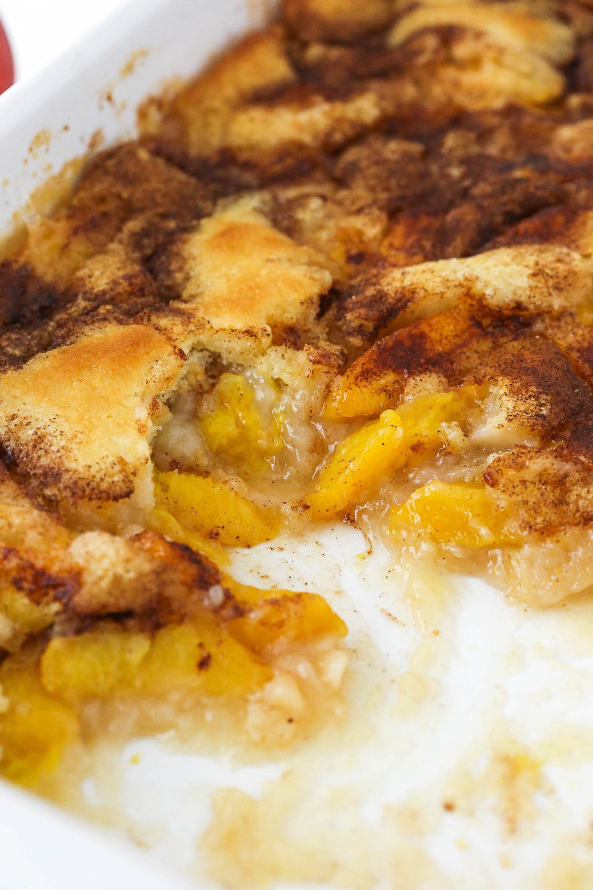 peach cobbler in white dish with several scoops removed