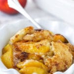 peach cobbler in white ruffle bowl with peach in background