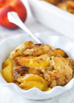 peach cobbler in white ruffle bowl with peach in background