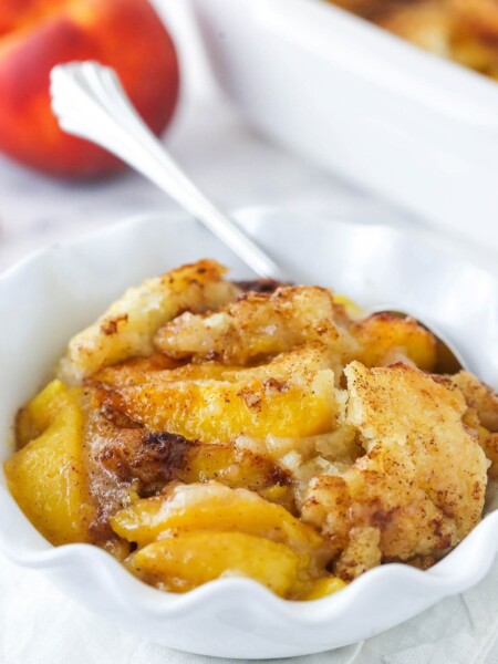 peach cobbler in white ruffle bowl with peach in background