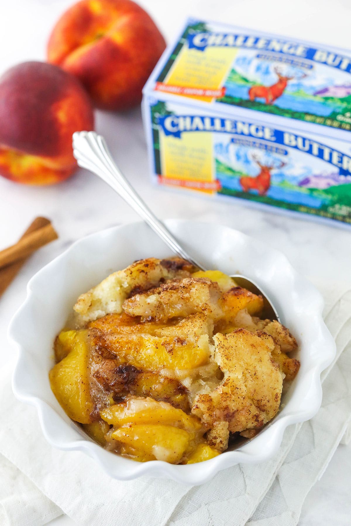 peach cobbler in white bowl with challenge butter in background