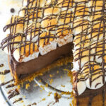 A marshmallow, chocolate and graham cracker cheesecake on a metal cake stand with one large slice removed