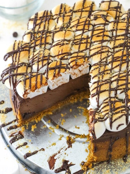 A marshmallow, chocolate and graham cracker cheesecake on a metal cake stand with one large slice removed