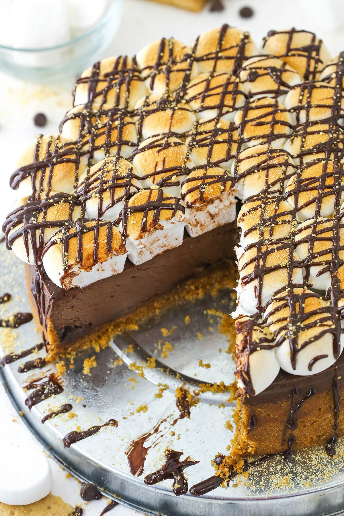 A marshmallow, chocolate and graham cracker cheesecake on a metal cake stand with one large slice removed