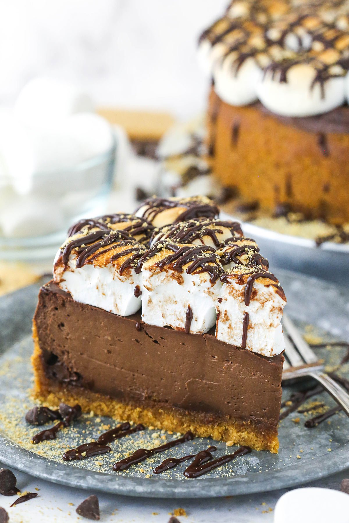 A slice of homemade chocolate smores cheesecake on a plate with the full cake in the background