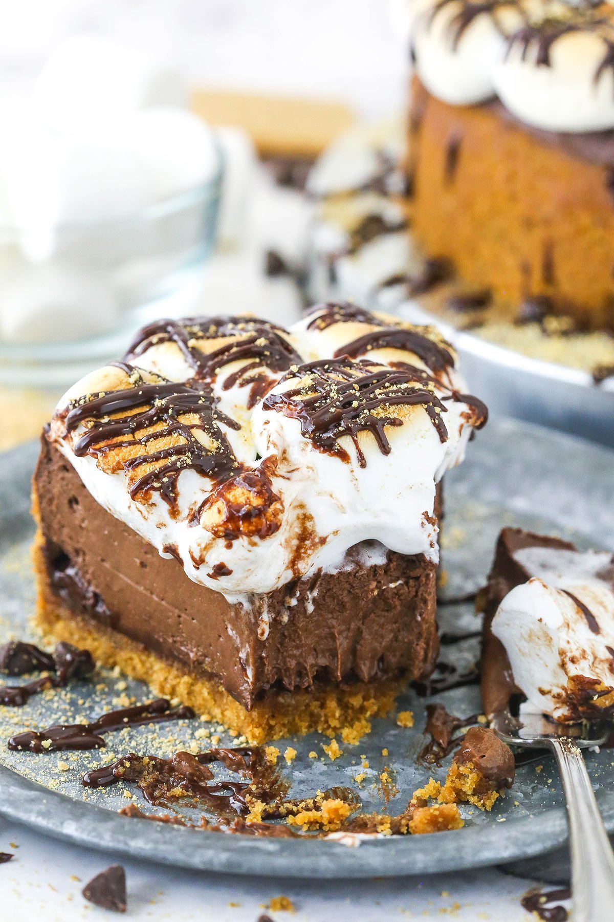 A half-eaten slice of smores cheesecake on a plate with one bite on a metal fork