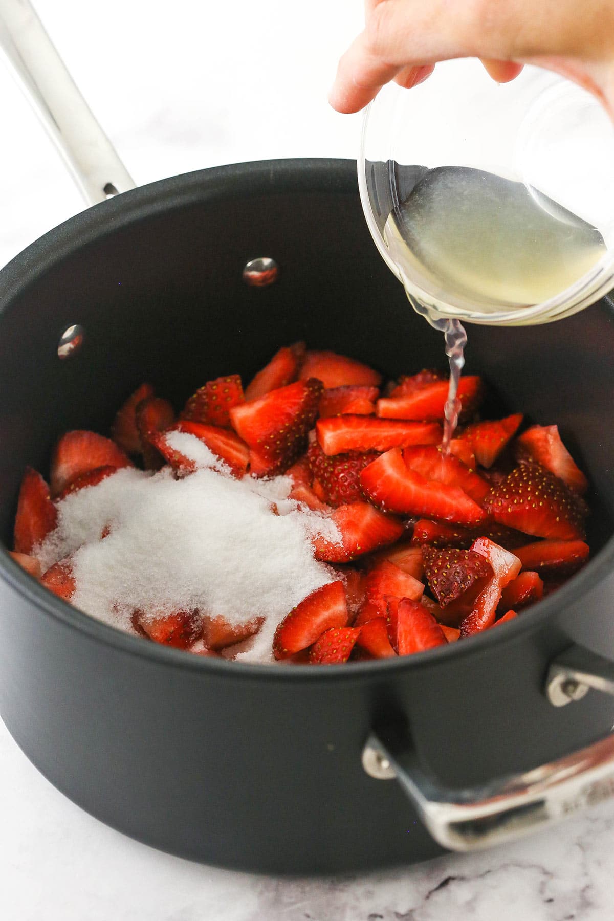 pouring lemon juice into pan filled with strawberries and sugar