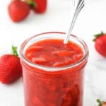 strawberry sauce in a clear jar with strawberries around it