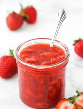 strawberry sauce in a clear jar with strawberries around it