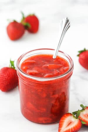 strawberry sauce in a clear jar with strawberries around it
