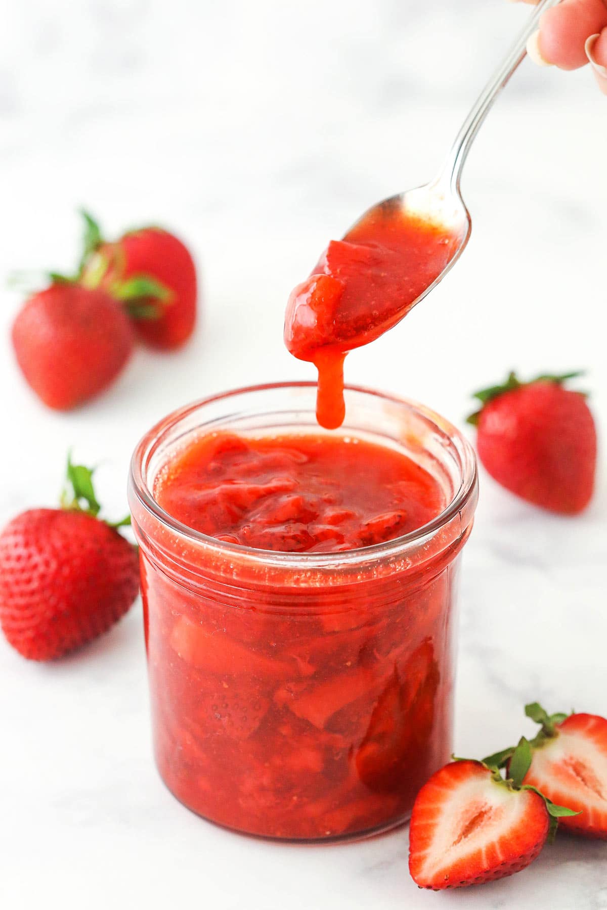 chunky strawberry sauce dripping off a spoon into clear jar