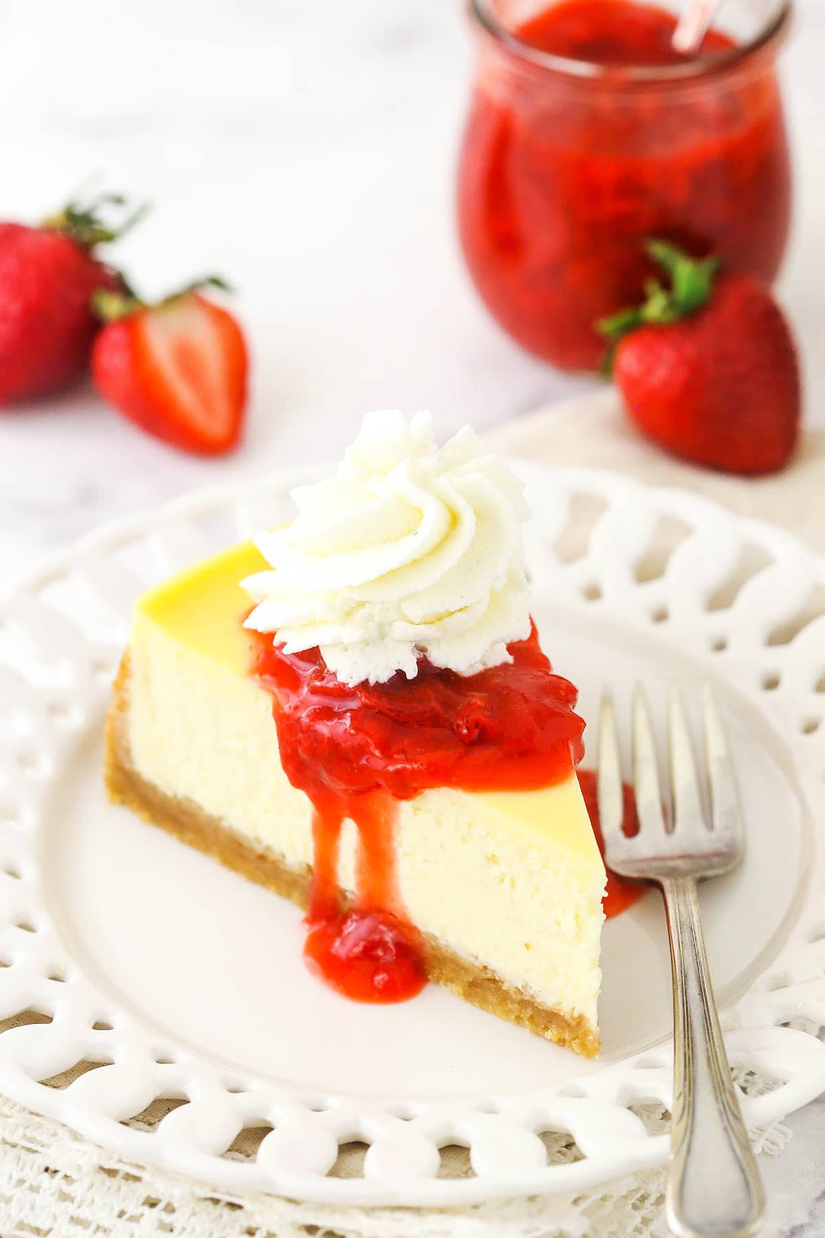 vanilla cheesecake on white plate with strawberry sauce on top and in a jar in the background