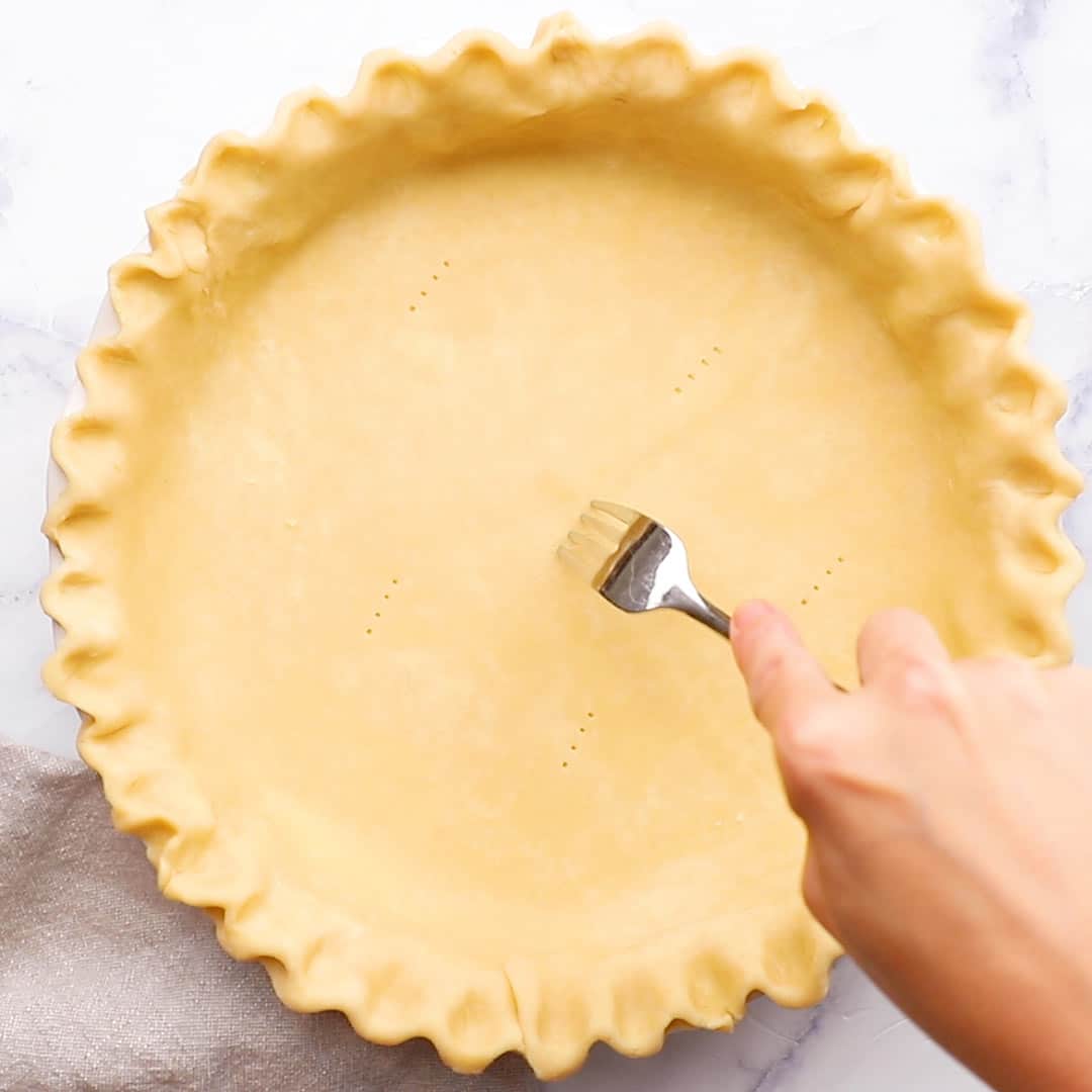 pie crust in pie pan with fork making pricks, on a marble table
