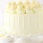 A white chocolate layer cake on a cake stand placed on a marble countertop