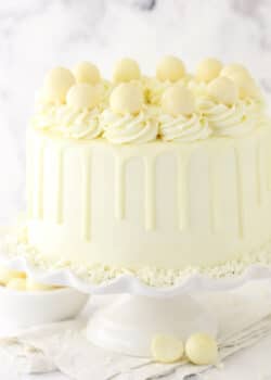 A white chocolate layer cake on a cake stand placed on a marble countertop