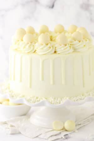 A white chocolate layer cake on a cake stand placed on a marble countertop