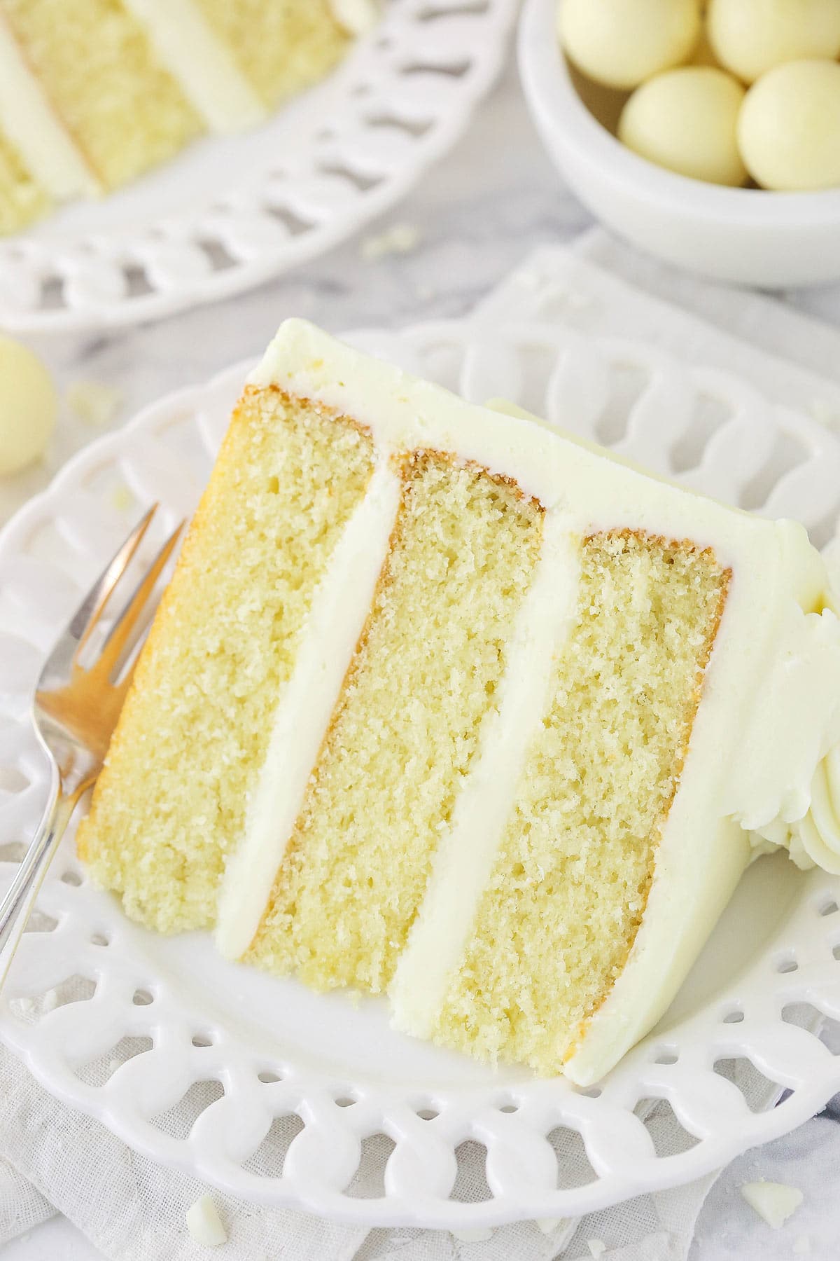 A piece of white chocolate layer cake on a plate with fancy cutouts in the rim