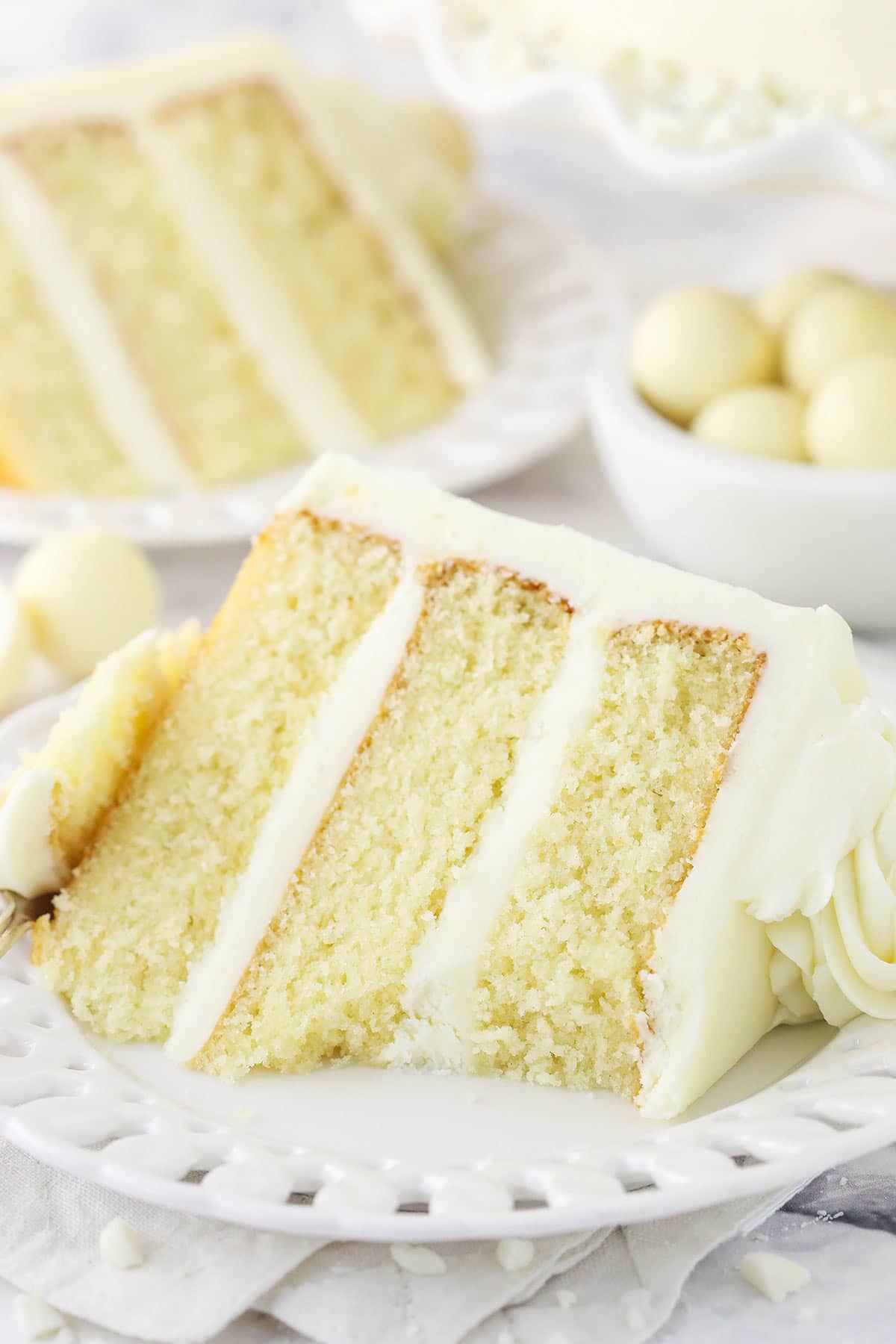 A slice of layer cake on a plate with one bite on a fork beside it