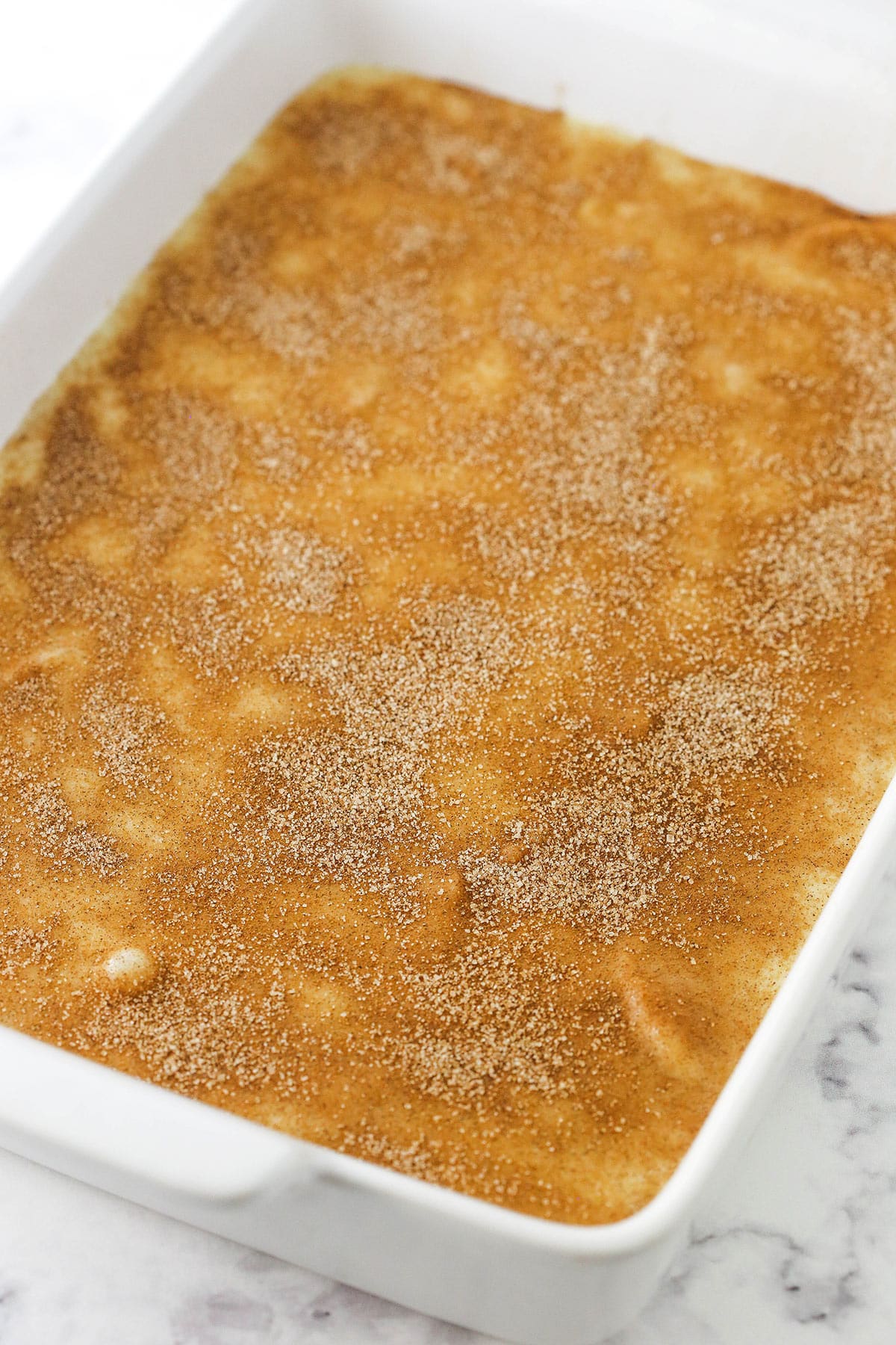 An unbaked apple cobbler inside of a white baking dish with handles.