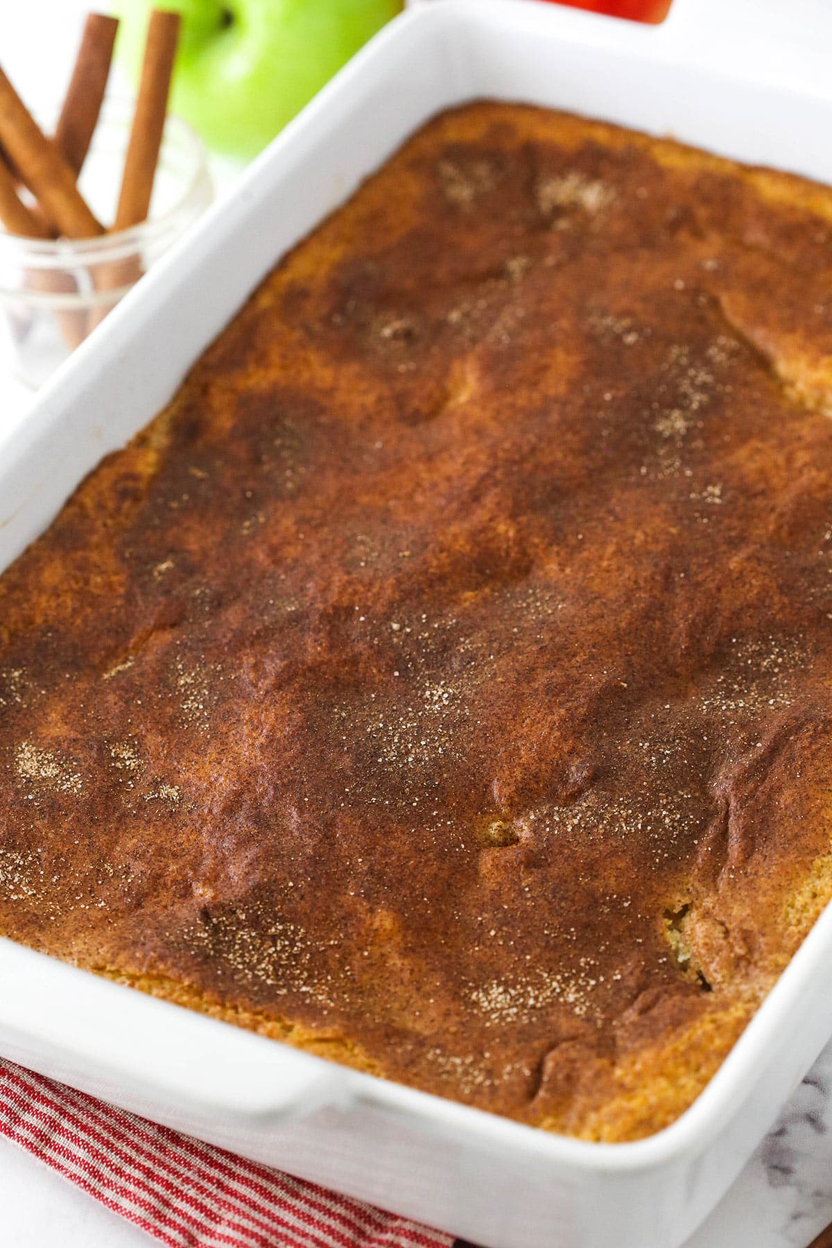 An apple cobbler in a baking dish with a jar of cinnamon sticks behind it.