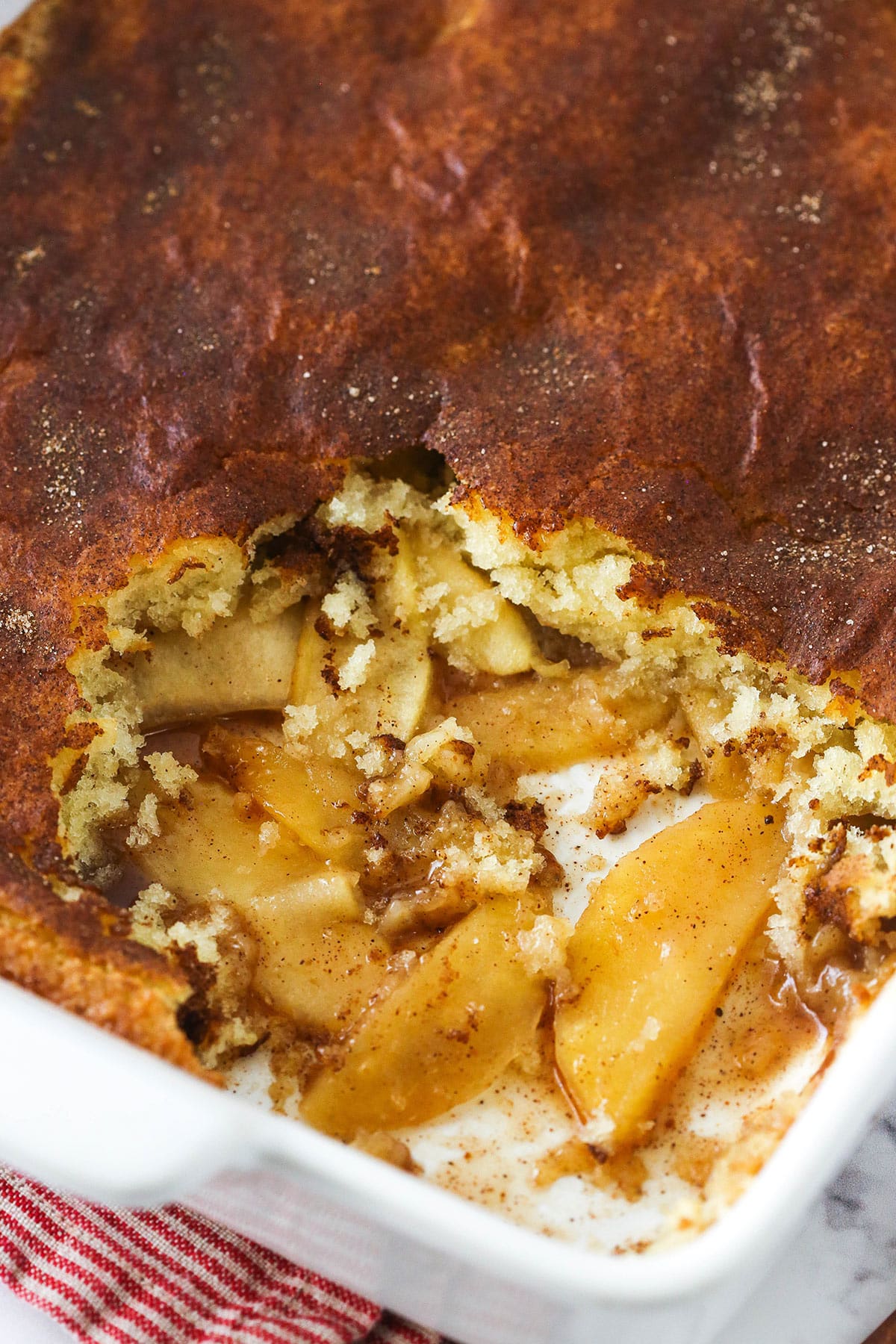 Freshly baked apple cobbler in a casserole dish with a couple of servings removed.