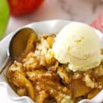 A close-up shot of apple cobbler in a bowl with two apples in the background