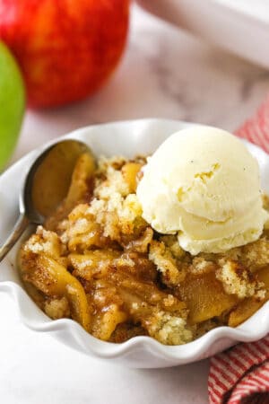 A close-up shot of apple cobbler in a bowl with two apples in the background