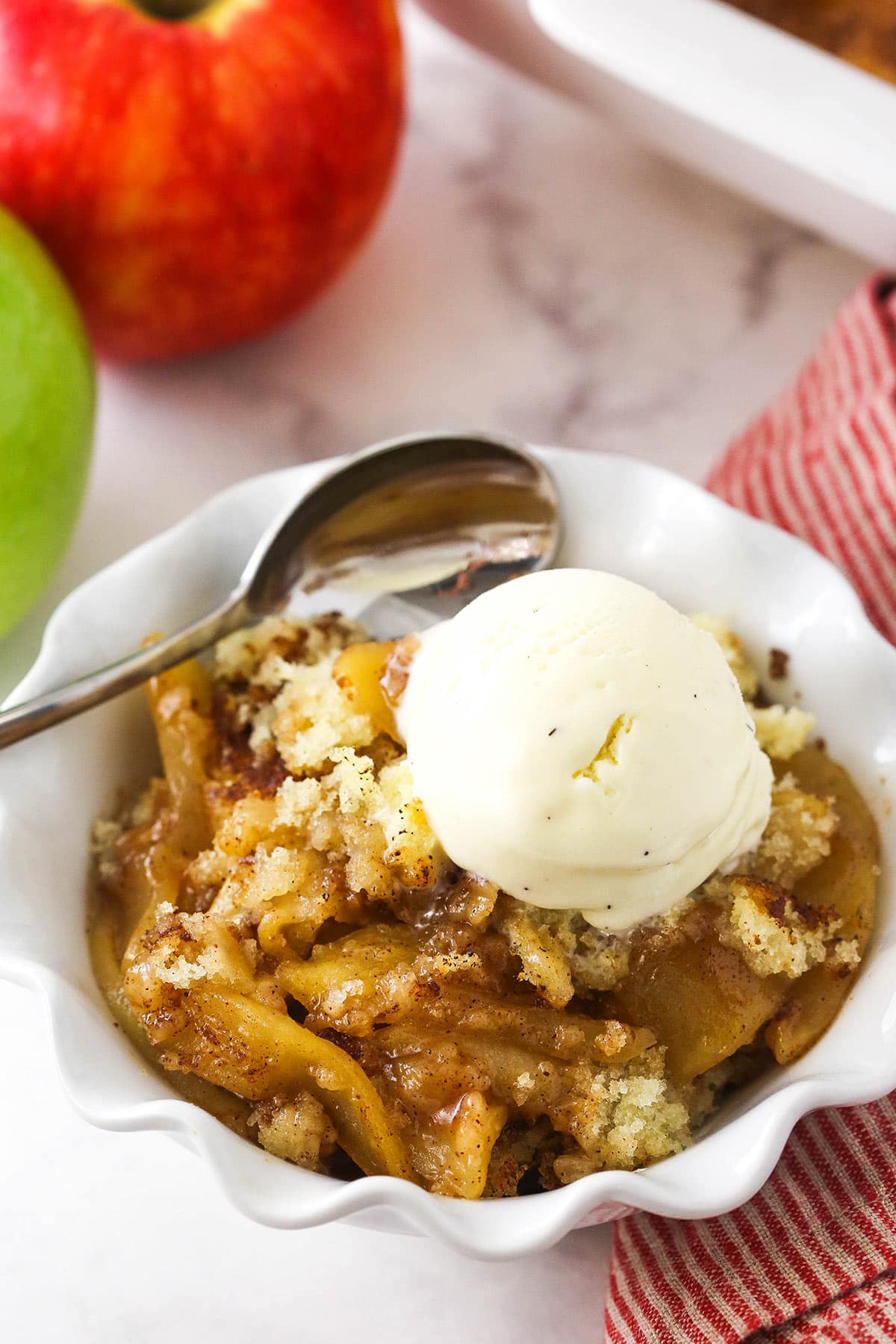 A serving of apple cobbler in a bowl with a spoon and a small scoop of ice cream.