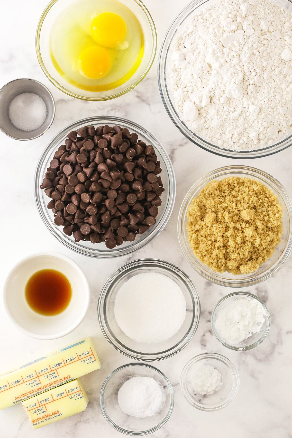 Vanilla extract, eggs, brown sugar, granulated sugar and the rest of the ingredients on a marble countertop.