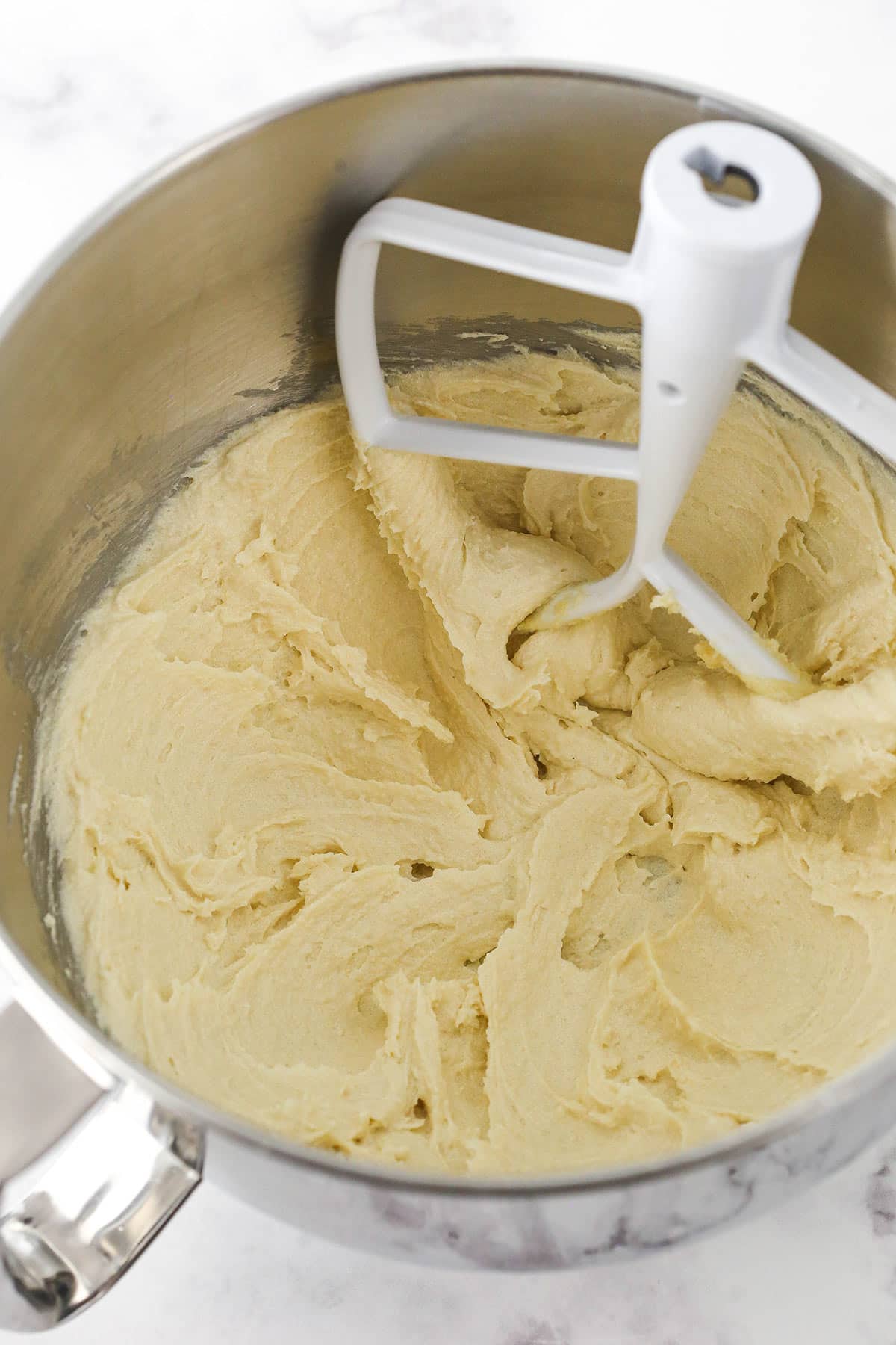 Creamed butter and sugar inside of a large metal mixing bowl with the whisk attachment inside.