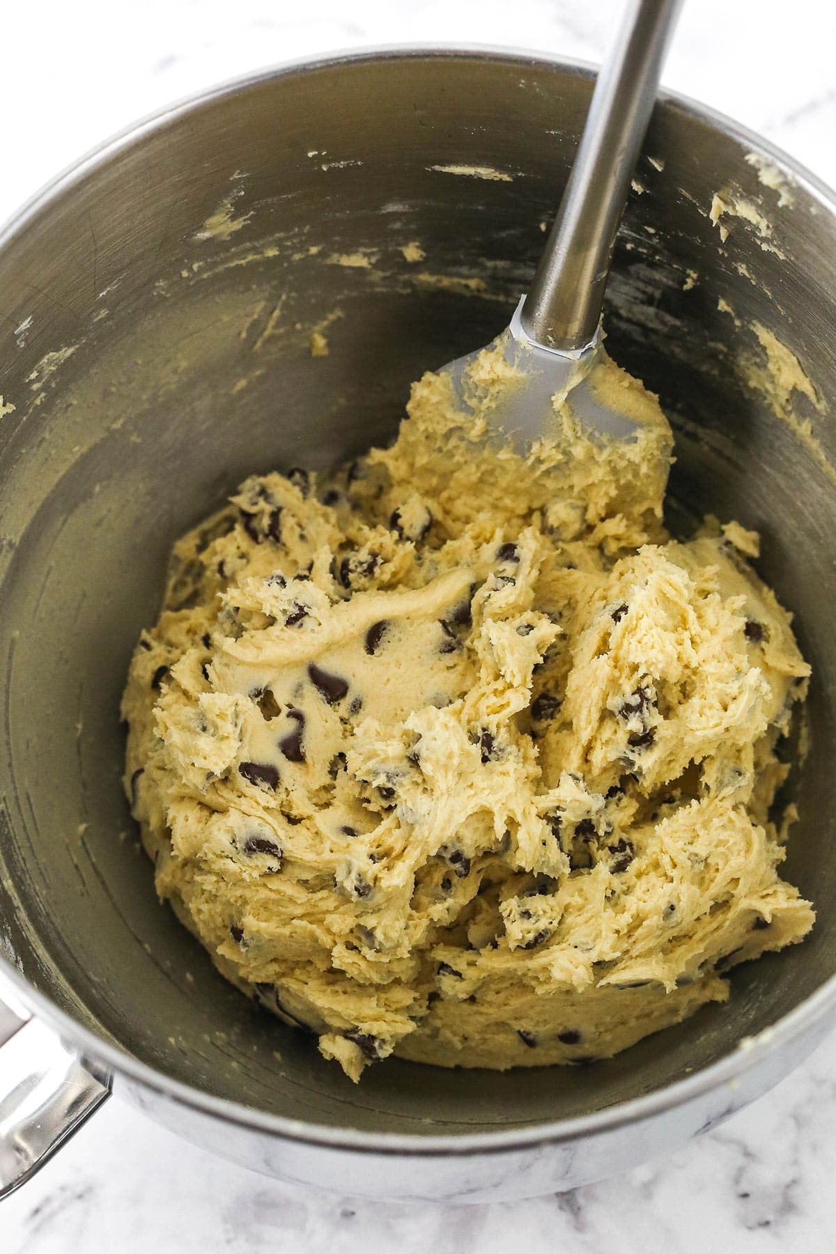 Completed chocolate chip cookie dough in a big metal bowl with a rubber spatula
