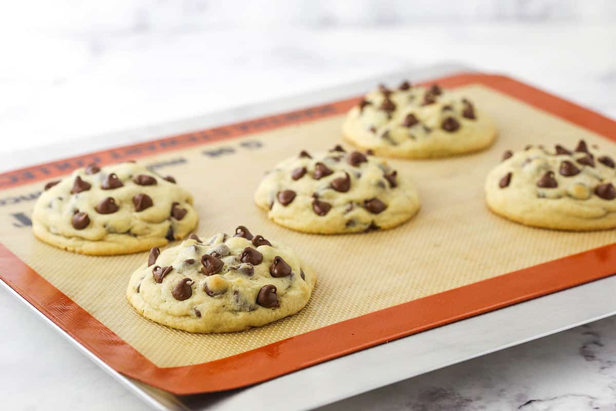 Five freshly baked cookies cooling on a lined baking sheet.