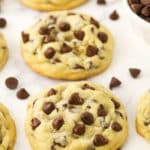 Homemade chocolate chip cookies lined up on a kitchen countertop with some loose chocolate chips