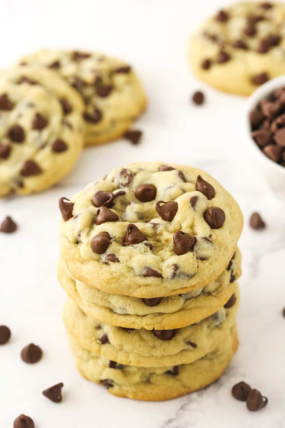A stack of four chocolate chip cookies on a white countertop with more cookies in the background.