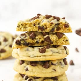 A pile of three chocolate chip cookies with two cookie halves balanced on top