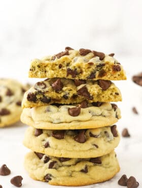 A pile of three chocolate chip cookies with two cookie halves balanced on top