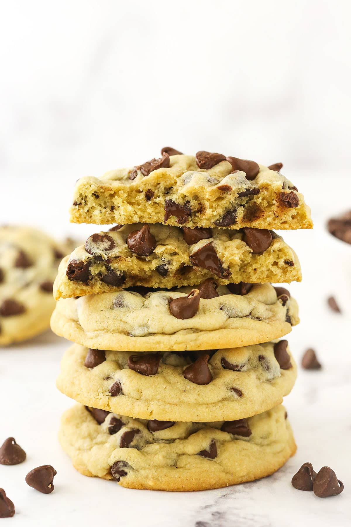 A pile of three chocolate chip cookies with two cookie halves balanced on top.