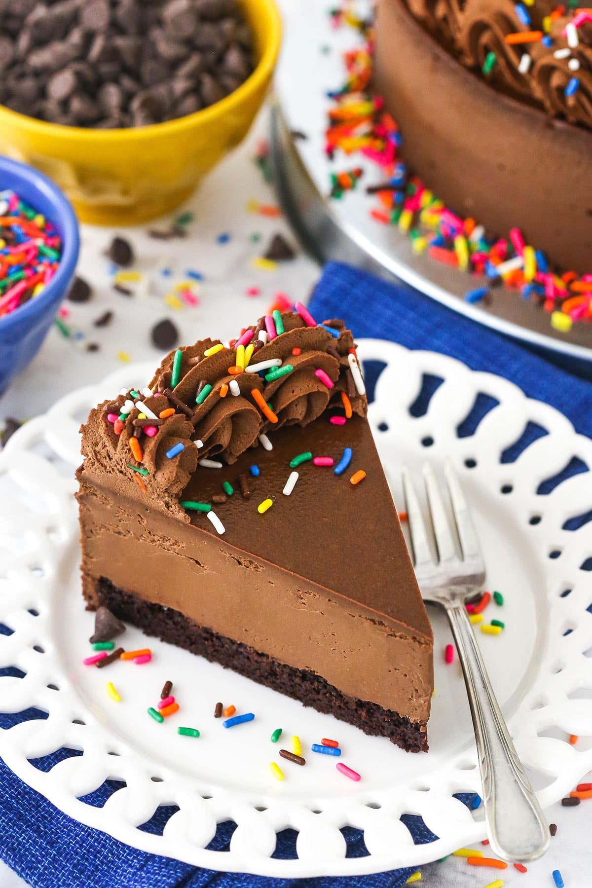 A slice of chocolate cheesecake on a plate with the remaining cheesecake behind it